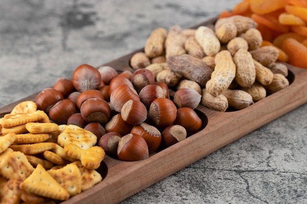 Cracker croccanti con nocciole e arachidi in guscio su una tavola di legno.