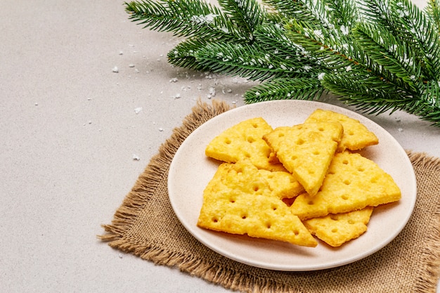 Cracker di formaggio festivo, concetto di snack di Capodanno. Biscotti, ramo di abete, neve artificiale, tovagliolo di tela di sacco.