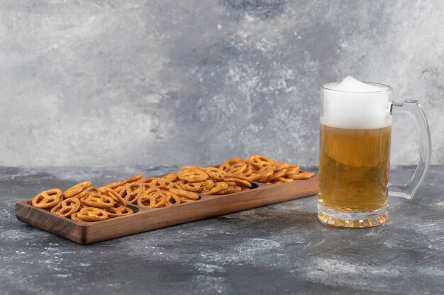 Cracker salato e secca delle ciambelline salate con boccale di birra di vetro posto sulla superficie di pietra