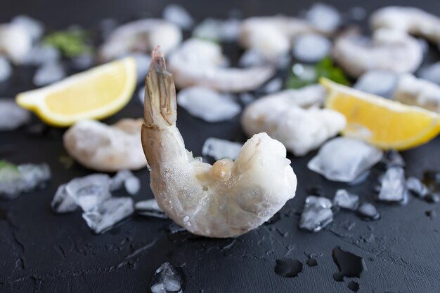 Crampe re congelate sullo sfondo sfocato con ghiaccio e limone Delizioso gambero senza testa per la preparazione del pasto Godetevi i frutti di mare naturali a basso contenuto di grassi e proteine Focus morbido in primo piano Closeup