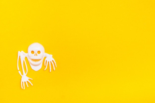 Cranio di plastica bianco con ossa su uno sfondo di cartone giallo. Illustrazione di Halloween pronta. Copia spazio