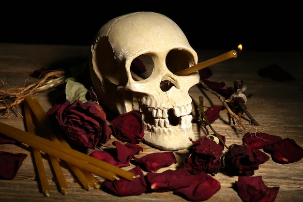 Cranio umano con petali di rosa secchi e candela sul primo piano della tavola di legno