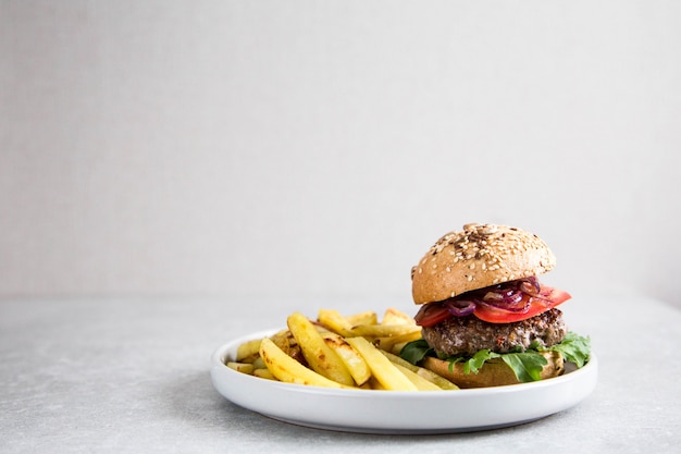 Crea hamburger di manzo fatti in casa e patatine fritte. Sfondo chiaro, copia spazio.