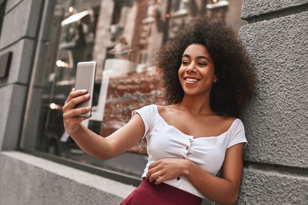 Creare ricordi felici attraente e giovane donna afroamericana che si fa selfie mentre trascorre del tempo