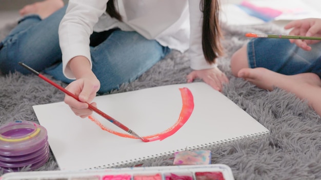 Creazione combinata per bambini in soggiorno mentre due ragazze dipingono con acquerelli e pennelli su un'enorme carta da disegno sul pavimento