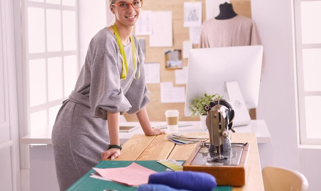 Creazione di nuovi stili alla moda Giovane donna allegra che cuce mentre è seduta al suo posto di lavoro in un laboratorio di moda