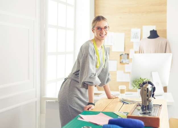 Creazione di nuovi stili alla moda Giovane donna allegra che cuce mentre è seduta al suo posto di lavoro in un laboratorio di moda