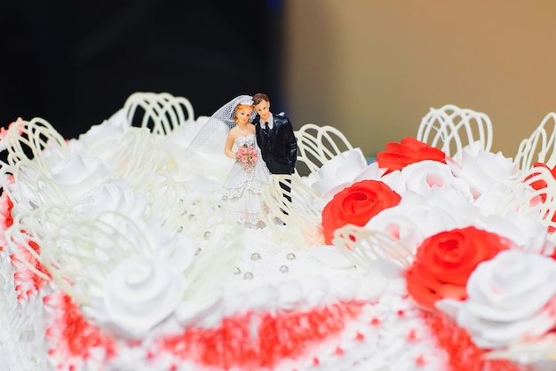 Crema bianca della torta nunziale decorata con le rose rosse con le figure della sposa e dello sposo