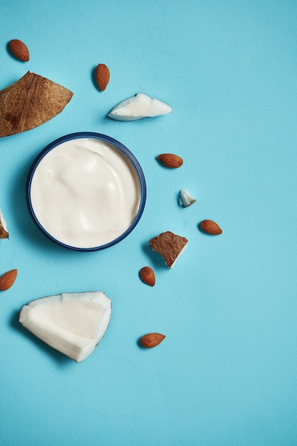 Crema bianca in un barattolo con cocco, mandorle su foglia blu e tropicale. concetto di bellezza e assistenza sanitaria. Piano minimalista disteso con spazio di copia. Vista dall'alto. Cura della pelle naturale cosmetica