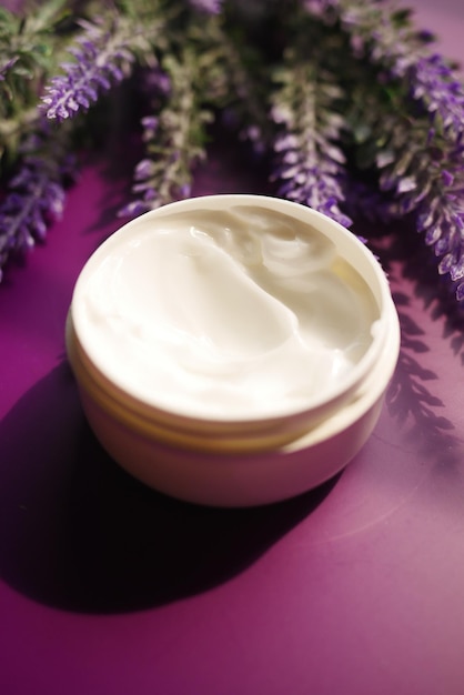 Crema cosmetica alle erbe in un contenitore e fiori di lavanda su sfondo viola