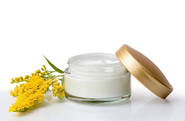 Crema cosmetica in un barattolo bianco. Con fiori gialli. Lozione curativa. Cura e igiene. Su uno sfondo bianco isolato.