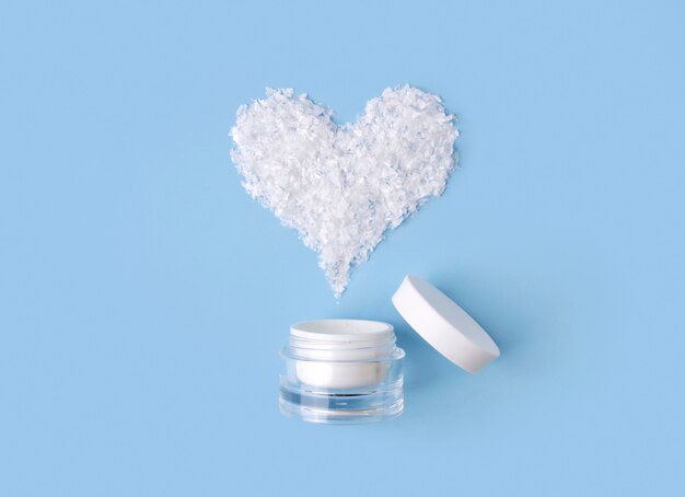 Crema cosmetica in una bottiglia con il cuore della neve sulla tavola blu