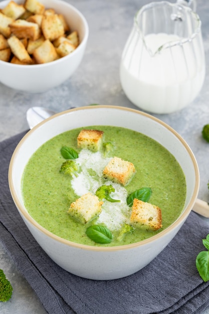 Crema di broccoli con basilico fresco e crostini di pane in una ciotola su fondo grigio cemento