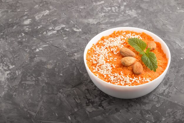 Crema di carote con semi di sesamo e mandorle in ciotola bianca. vista laterale, copyspace.