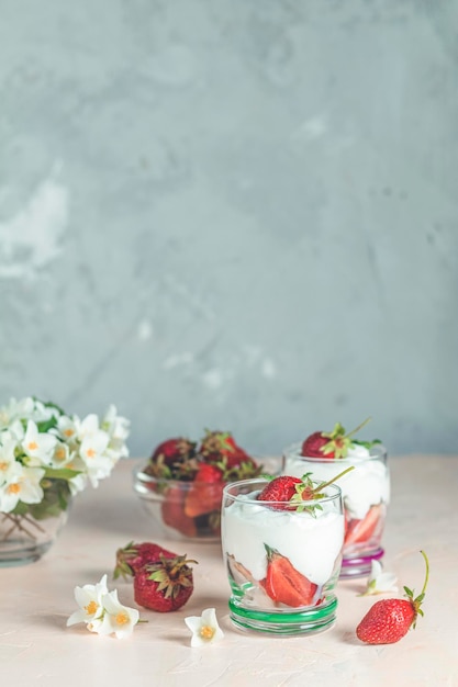 Crema di fragole Ciotola di vetro di fragole con panna montata e menta Fiori di gelsomino Superficie in cemento copia spazio per te testo