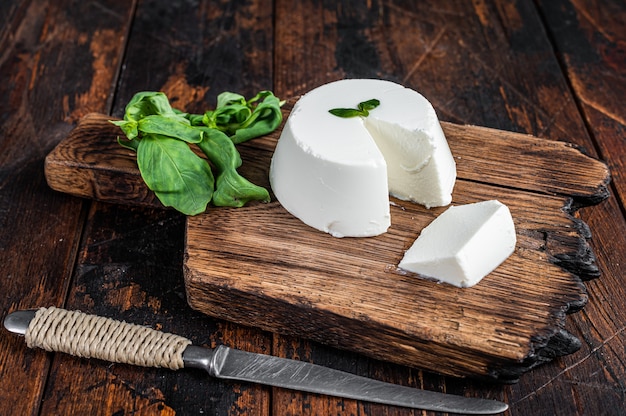 Crema di ricotta fresca su tavola di legno con basilico. Fondo in legno scuro. Vista dall'alto.