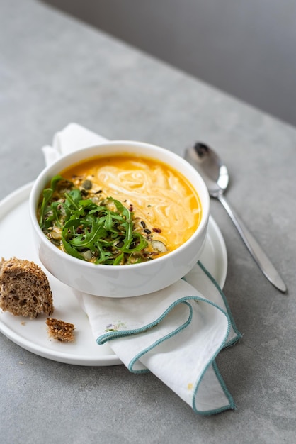 Crema di zuppa di carote in una ciotola bianca Ciotola di zuppa di carote con foglie di rucola sul tavolo di cemento