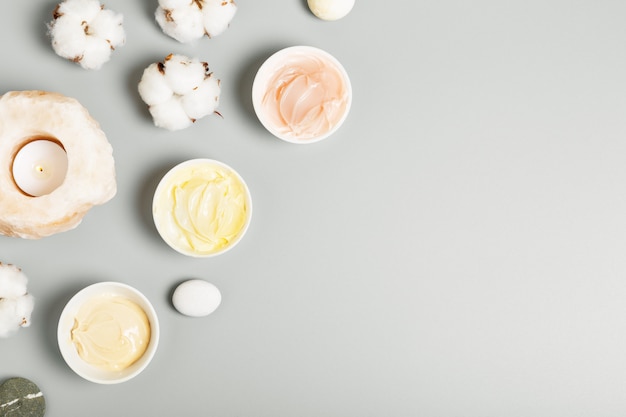 Crema gialla, rosa e beige, candele e cotone su fondo grigio. Il concetto di cosmetici naturali e bellezza.