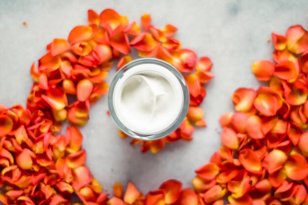 Crema idratante per il viso di bellezza e petali di fiori su prodotto cosmetico di lusso in marmo