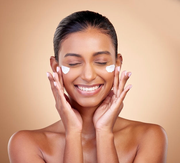 Crema per il viso cura della pelle sorriso della donna per la lucentezza estetica cosmetici o dermatologia pulita sullo sfondo dello studio felice modella femminile indiana lozione per il viso o crema solare per il bagliore di bellezza sana