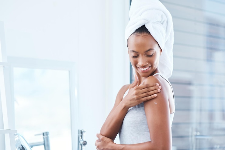 Foto crema per la spalla e per il corpo per la cura della pelle in bagno o in casa per l'idratazione, il bagliore o la lucentezza naturale. sorriso di donna felice e persona femminile con cosmetici, asciugamano e lozione per l'eczema per risultati di bellezza.