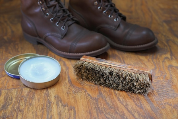 crema per scarpe e spazzola sul pavimento di legno contro stivali di pelle, pulizia e spazzolatura delle scarpe