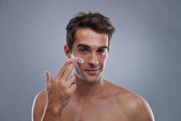 Crema ritratto e uomo con cura della pelle lucentezza e bellezza con luminosità su sfondo grigio studio Applicare persona e modello con routine mattutina o trattamento con lozione o umidità con benessere o viso