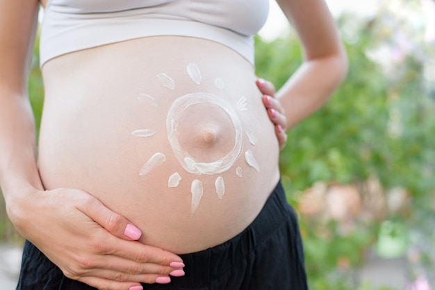 Crema solare dipinta su una pancia femminile incinta. Incinta . Avvicinamento