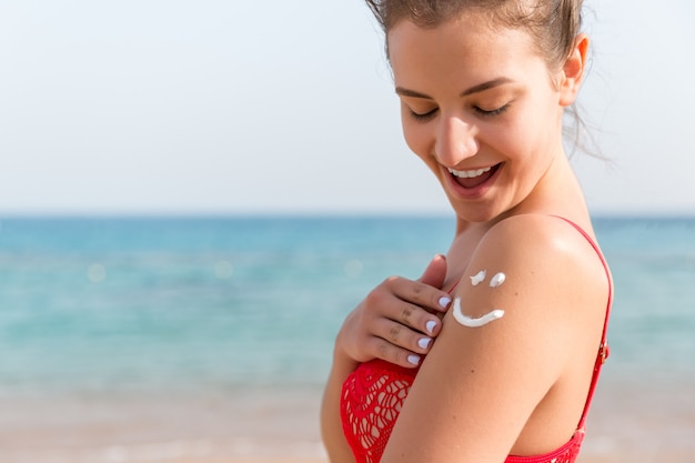 Crema solare sulla spalla della donna abbronzata a forma di viso sorridente.