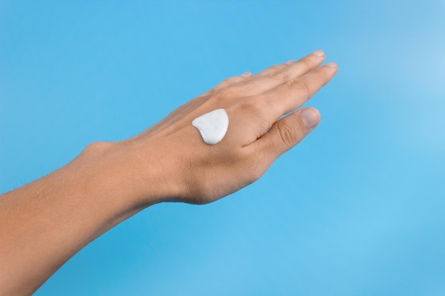 Crema sulla mano di una donna su un primo piano di sfondo blu. Concetto di cura della pelle. Pubblicità di cosmetici.