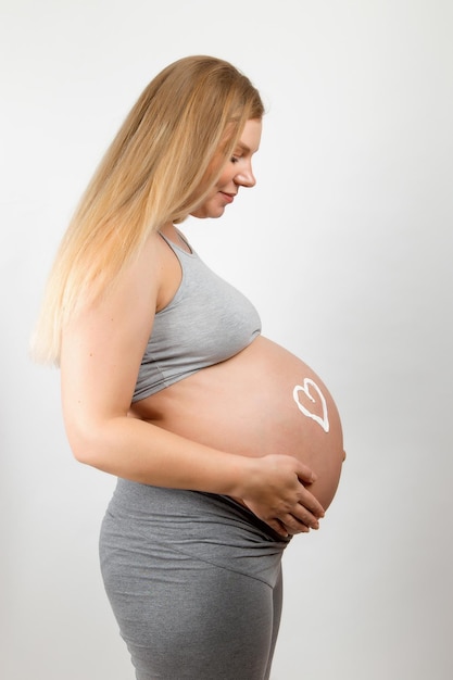 Crema sullo stomaco di una ragazza incinta a forma di cuore Cura della pelle per una donna incinta