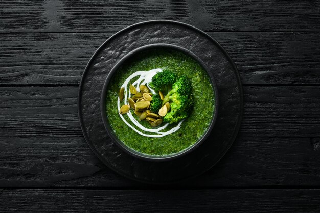 Crema verde di zuppa di broccoli e semi di zucca in una ciotola nera Vista dall'alto Spazio libero per il testo Stile rustico
