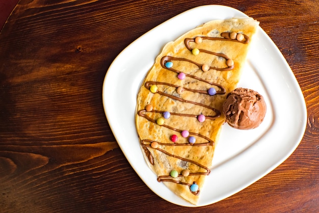 Crepe dolce con crema al cioccolato e gelato su fondo in legno