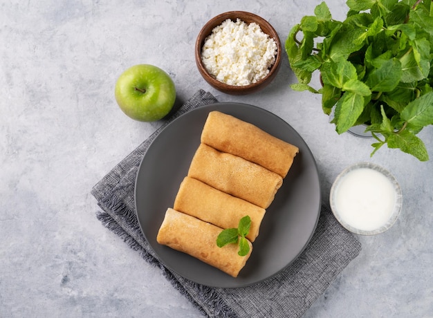 Crepe fatte in casa con formaggio cottage e mela su un piatto su uno sfondo blu con crema acida e menta Cibo sano per la colazione