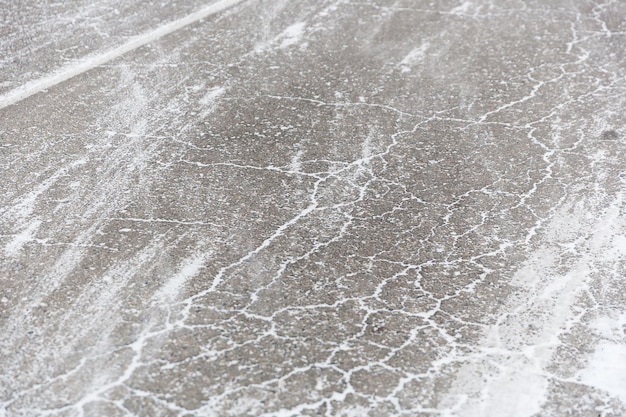 Crepe sull'asfalto pieno di neve. Bassa neve alla deriva su uno sfondo di texture di strada invernale