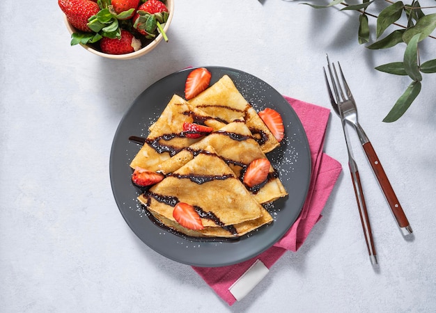 Crepes dolci con fragole fresche e cioccolato su un piatto grigio su sfondo chiaro Il concetto di cibo sano fatto in casa