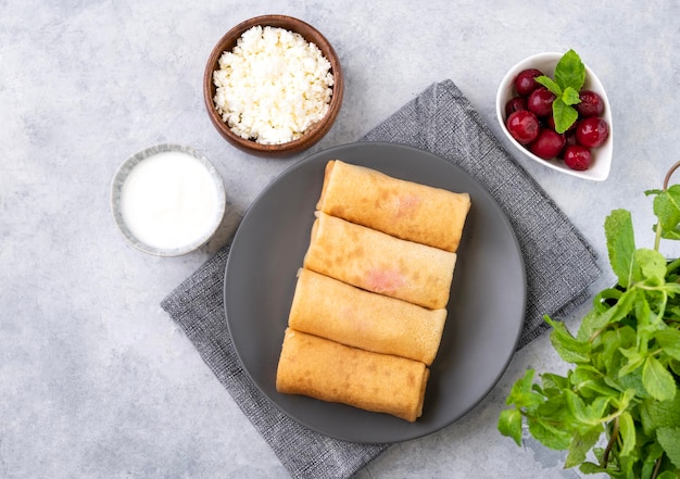 Crepes fatte in casa con bacche di chery e ricotta su un piatto su sfondo blu con panna acida Cibo sano per la colazione