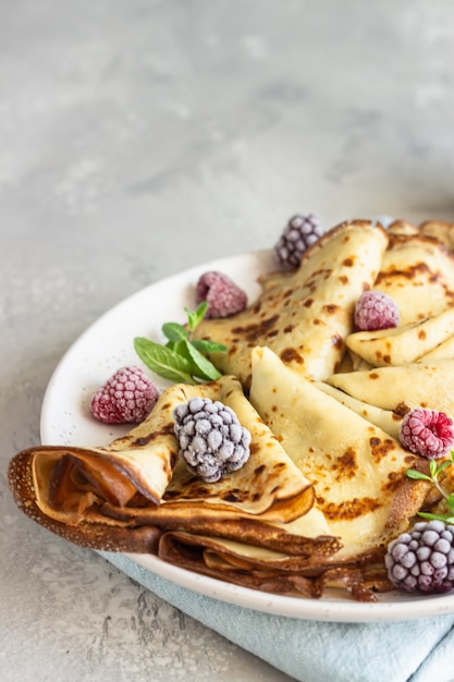 Crepes francesi appena fatte (pancake sottili) con frutti di bosco congelati e menta per colazione