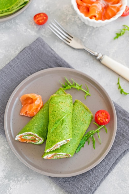 Crepes o frittelle di spinaci verdi con salmone affumicato e formaggio a pasta molle su sfondo grigio Spazio di copia