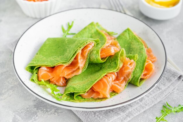 Crepes o frittelle di spinaci verdi con salmone affumicato e formaggio a pasta molle su un piatto