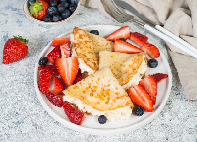 Crepes sottili con ricotta e fragole fresche su uno sfondo grigio cemento.