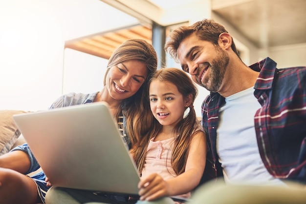 Crescere in un mondo connesso Foto di una madre e un padre che usano un laptop con la figlia sul divano di casa