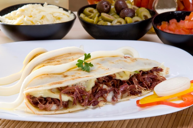 Crespelle di carne seccata al sole con ingredienti olive, formaggio, pomodoro, su fondo.