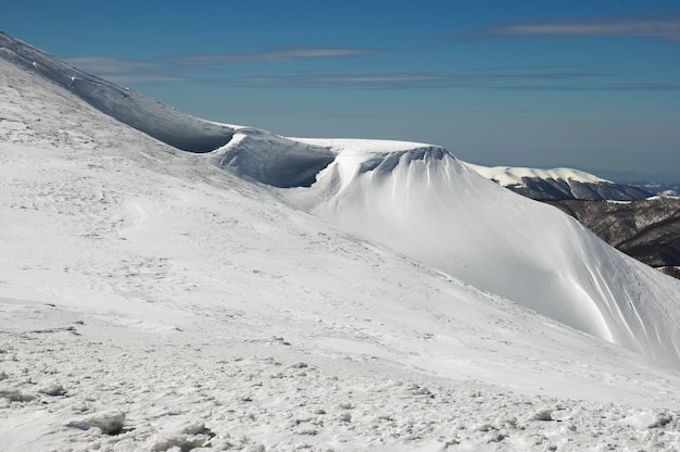 Cresta delle montagne invernali con cappucci di neve a sbalzo e piste da snowboard su sk blu