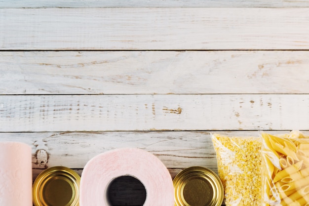 Crisi alimentare di quarantena delle forniture alimentari isolata su fondo di legno bianco. Riso, pasta, corn flakes, carta igienica, cibo in scatola. Concetto di consegna del cibo, donazione, beneficenza. Copyspace.