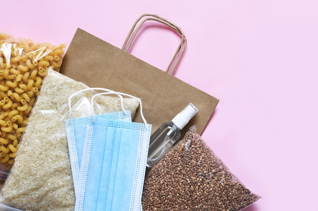 Crisi delle forniture alimentari su sfondo rosa. Pasta, grano saraceno, maschera, antisettico, carta. Donazione. Piattamente cibo.