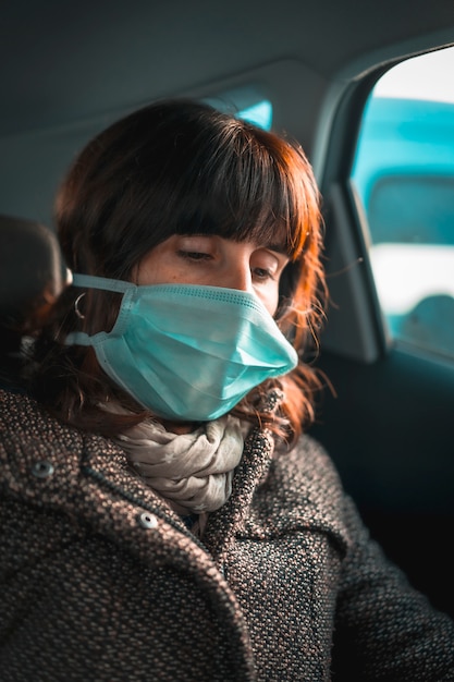 Crisi sanitaria, una giovane donna caucasica che legge un libro elettronico con una maschera in un'auto nella quarantena covid-19