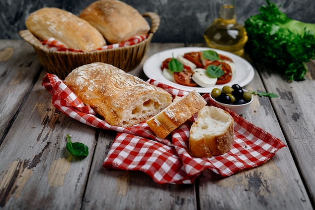 Croccante ciabatta italiana con insalata caprese fresca, olive ed erbe su un tovagliolo a quadretti