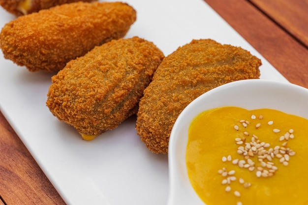 Crocchette fritte con salsa gialla sulla vista laterale del piatto bianco su fondo di legno