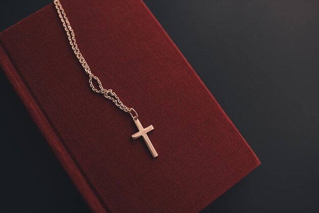Croce cristiana d'argento sul libro della Bibbia di carta rossa sul tavolo